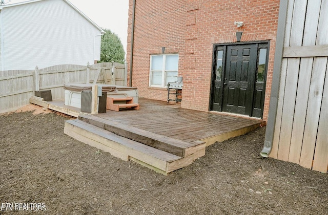 entrance to property with a deck, brick siding, fence, and a hot tub