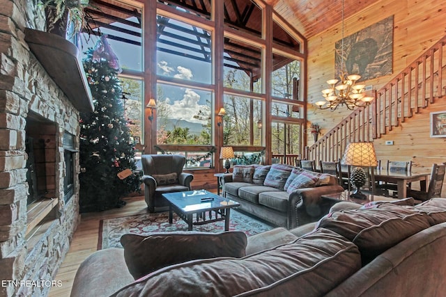 living room with wood finished floors, an inviting chandelier, stairs, a stone fireplace, and wood walls