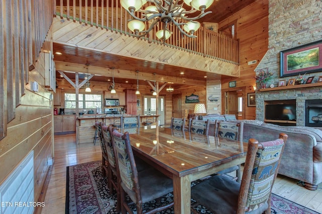 dining room featuring wood walls, a fireplace, a towering ceiling, light wood-type flooring, and an inviting chandelier