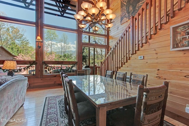 dining room with a healthy amount of sunlight, wood walls, wood-type flooring, and a notable chandelier