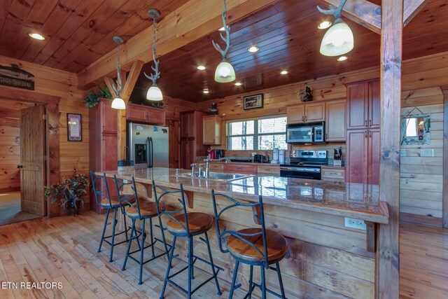 kitchen with wooden ceiling, wooden walls, a sink, appliances with stainless steel finishes, and a kitchen bar