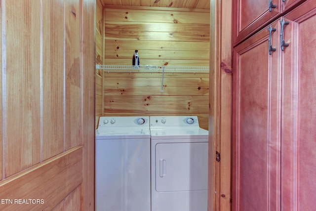 washroom with cabinet space, wood walls, and washing machine and clothes dryer