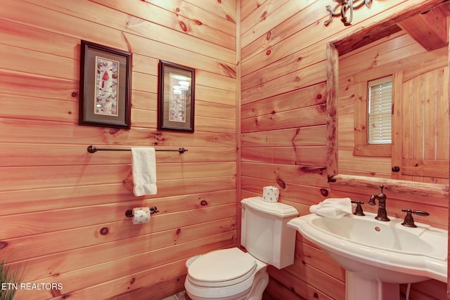 bathroom featuring a sink, wood walls, and toilet