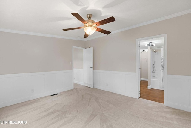 carpeted empty room with a wainscoted wall, ornamental molding, and a ceiling fan