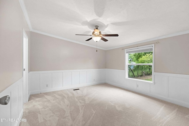 carpeted empty room with wainscoting, crown molding, a textured ceiling, and ceiling fan