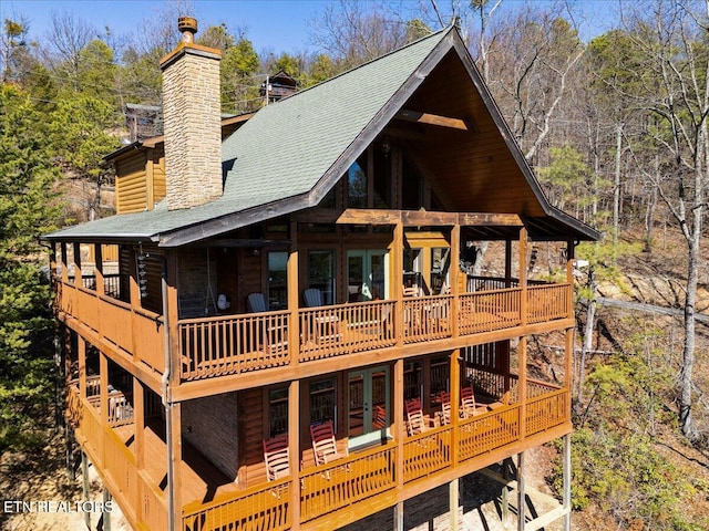 rear view of house featuring french doors, a chimney, a shingled roof, and a wooden deck