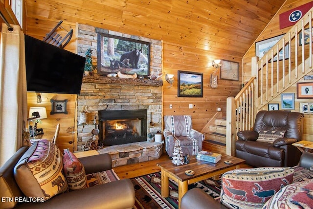 living area with stairway, a stone fireplace, vaulted ceiling, and wooden walls