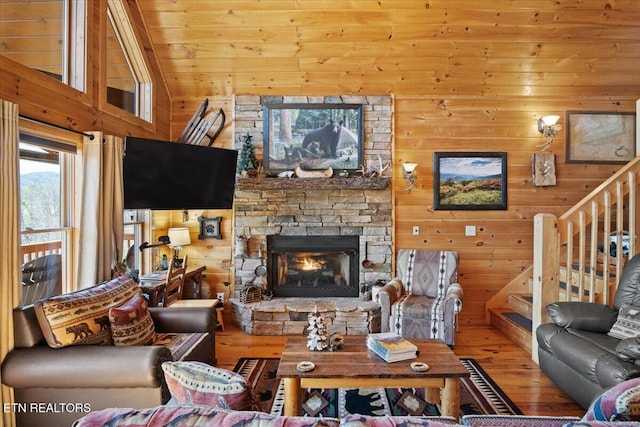 living room featuring a stone fireplace, wooden walls, wood finished floors, vaulted ceiling, and stairway