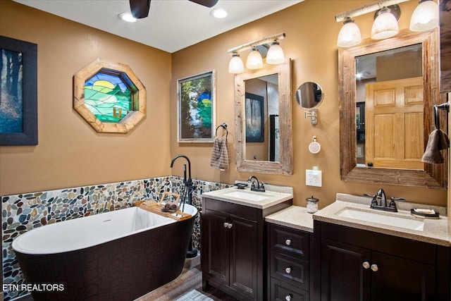 full bathroom featuring a ceiling fan, a soaking tub, two vanities, and a sink