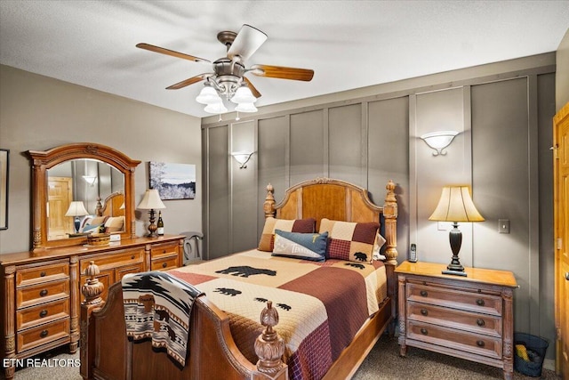 bedroom featuring a ceiling fan, dark colored carpet, and a decorative wall