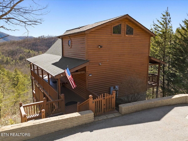 view of property exterior with a forest view, roof with shingles, and faux log siding