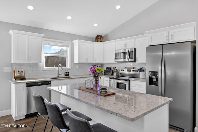 kitchen featuring a breakfast bar area, stainless steel appliances, a sink, white cabinetry, and vaulted ceiling