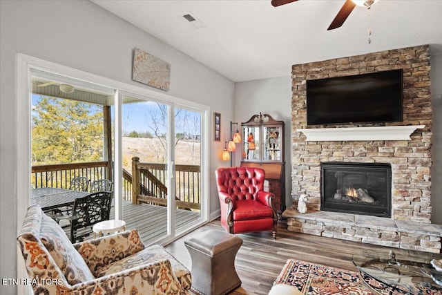 living area with a ceiling fan, a fireplace, visible vents, and wood finished floors