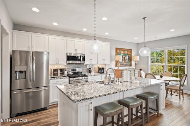 kitchen with white cabinets, decorative backsplash, wood finished floors, stainless steel appliances, and a sink