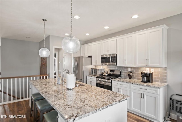 kitchen with tasteful backsplash, dark wood finished floors, an island with sink, appliances with stainless steel finishes, and a sink