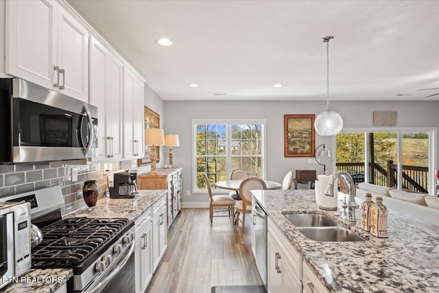 kitchen featuring light wood finished floors, backsplash, appliances with stainless steel finishes, white cabinets, and a sink