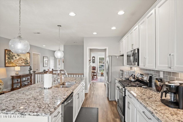 kitchen with light wood finished floors, appliances with stainless steel finishes, white cabinetry, a sink, and an island with sink