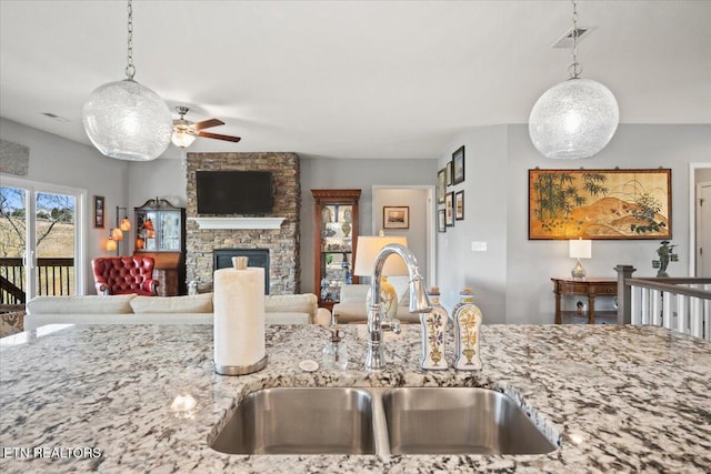 kitchen with light stone counters, a fireplace, visible vents, hanging light fixtures, and a sink