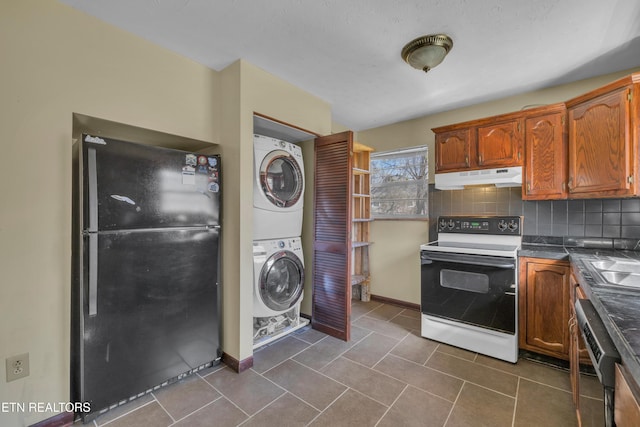 kitchen featuring white electric range oven, dark countertops, stacked washer / drying machine, freestanding refrigerator, and under cabinet range hood