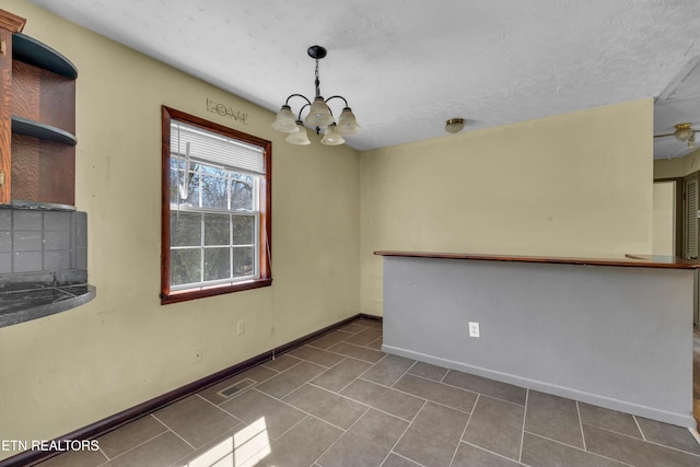 unfurnished dining area featuring visible vents, an inviting chandelier, a textured ceiling, tile patterned flooring, and baseboards