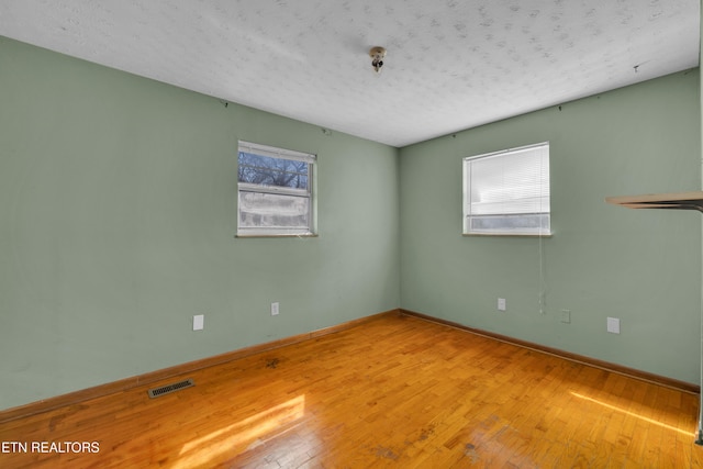 empty room featuring baseboards, a textured ceiling, visible vents, and wood finished floors