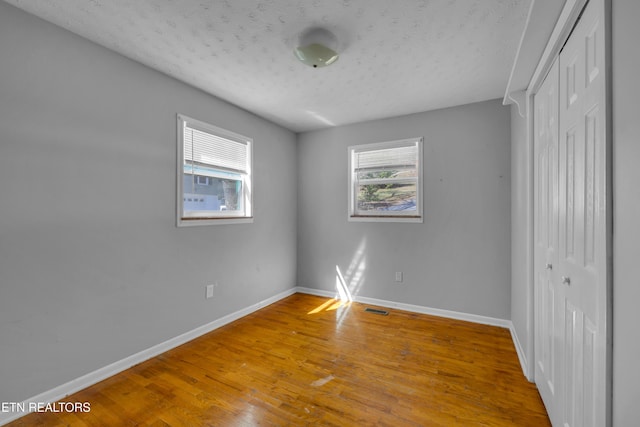 unfurnished bedroom with a textured ceiling, wood finished floors, visible vents, baseboards, and a closet