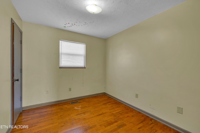 unfurnished room featuring visible vents, a textured ceiling, baseboards, and wood finished floors