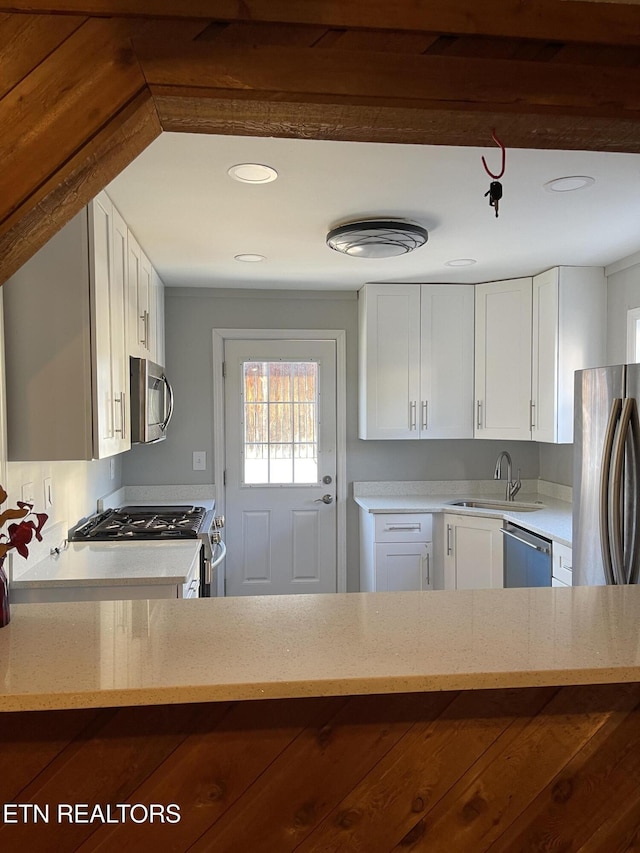 kitchen with appliances with stainless steel finishes, white cabinets, a sink, and light stone countertops