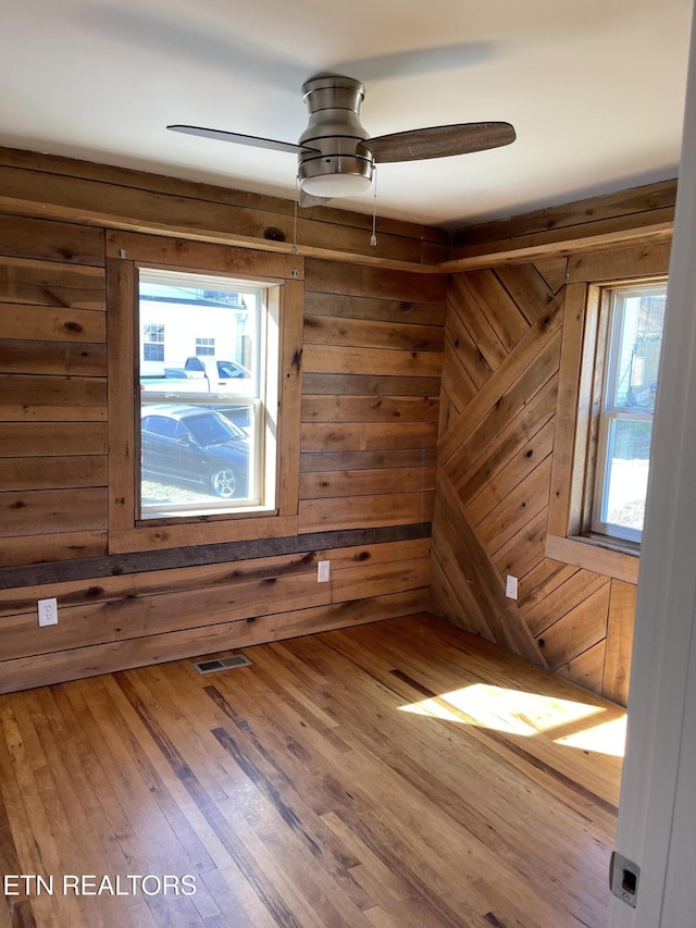 unfurnished room with hardwood / wood-style flooring, plenty of natural light, wooden walls, and a ceiling fan