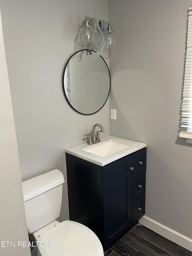 half bath with baseboards, vanity, toilet, and wood finished floors