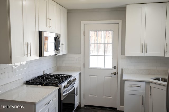 kitchen with appliances with stainless steel finishes, white cabinets, backsplash, and light stone countertops