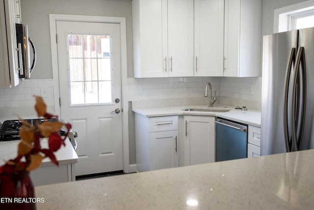 kitchen with backsplash, appliances with stainless steel finishes, white cabinets, a sink, and light stone countertops