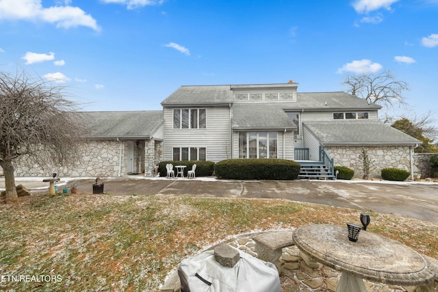 back of house with stone siding, a patio, and roof with shingles