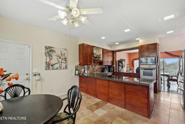 kitchen featuring stainless steel appliances, dark countertops, backsplash, a ceiling fan, and a peninsula