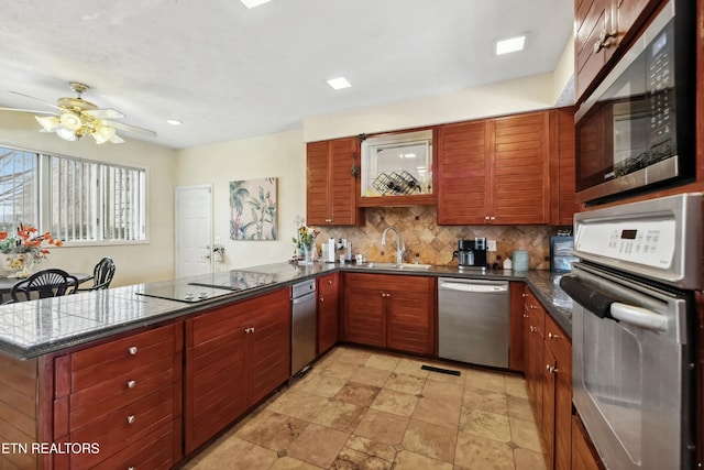 kitchen with stainless steel appliances, dark countertops, backsplash, a sink, and a peninsula