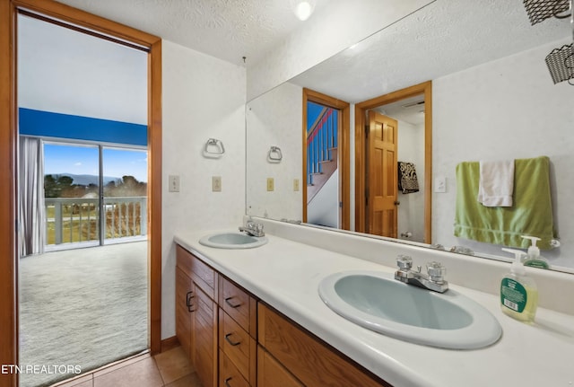 full bathroom featuring a textured ceiling, double vanity, a sink, and tile patterned floors