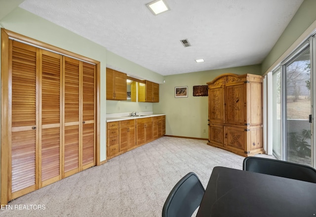 kitchen with light countertops, visible vents, brown cabinetry, light carpet, and baseboards