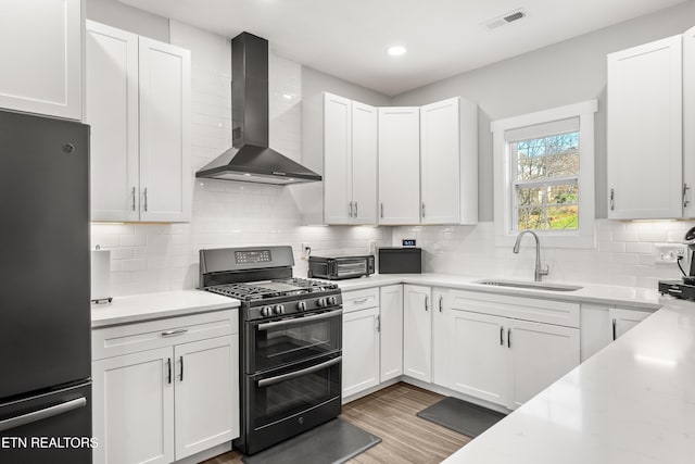 kitchen with visible vents, wall chimney exhaust hood, freestanding refrigerator, double oven range, and a sink