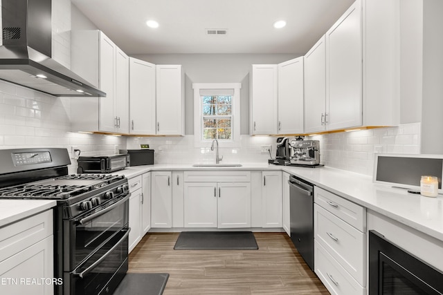 kitchen with wall chimney exhaust hood, light countertops, visible vents, a sink, and black appliances