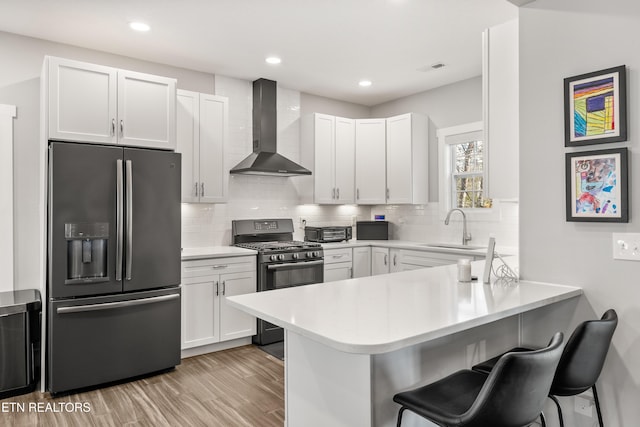 kitchen with wall chimney exhaust hood, stainless steel appliances, a sink, a peninsula, and a kitchen breakfast bar