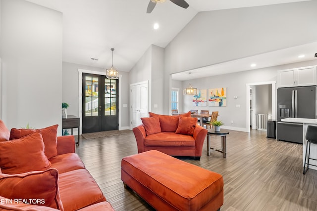 living area with high vaulted ceiling, wood finished floors, visible vents, and baseboards