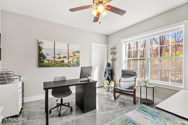 office space featuring finished concrete floors, ceiling fan, and baseboards