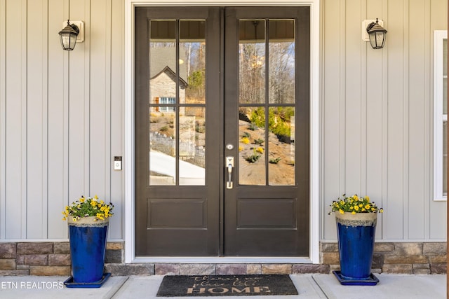 view of exterior entry featuring stone siding, board and batten siding, and french doors