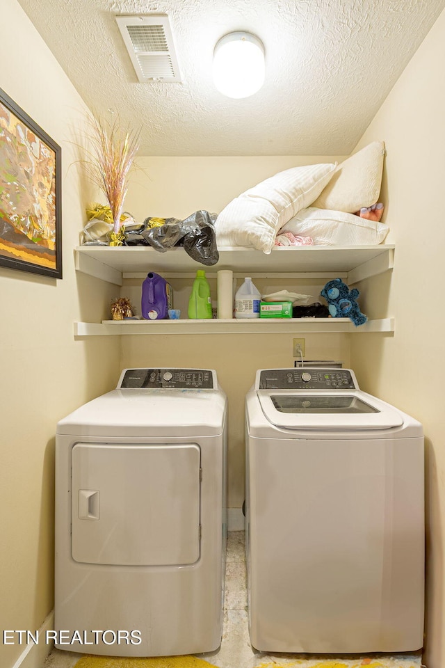 clothes washing area with laundry area, visible vents, a textured ceiling, and washing machine and clothes dryer