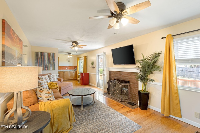 living area featuring a brick fireplace, wood finished floors, a ceiling fan, and baseboards