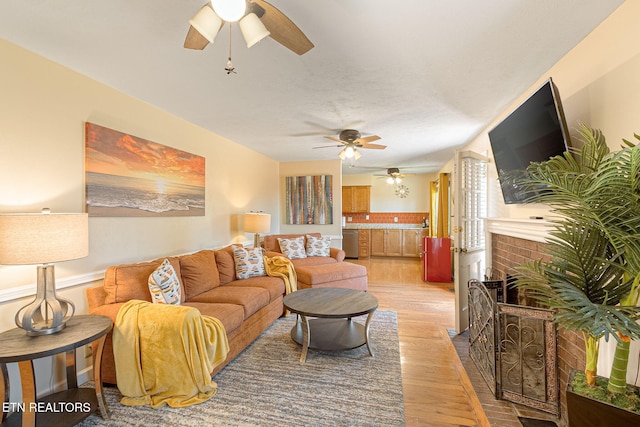 living room with a fireplace, light wood-style flooring, and ceiling fan