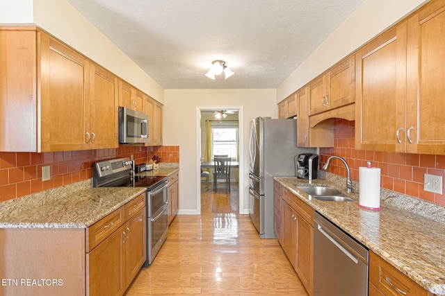 kitchen featuring stainless steel appliances, decorative backsplash, light wood-style floors, a sink, and light stone countertops