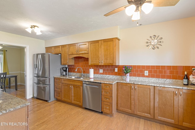 kitchen featuring stainless steel appliances, light wood-style floors, brown cabinetry, and a sink