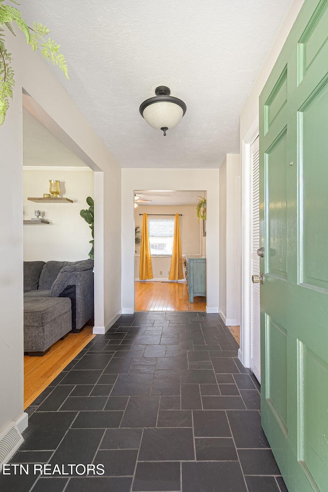 hall featuring a textured ceiling, stone finish flooring, visible vents, and baseboards