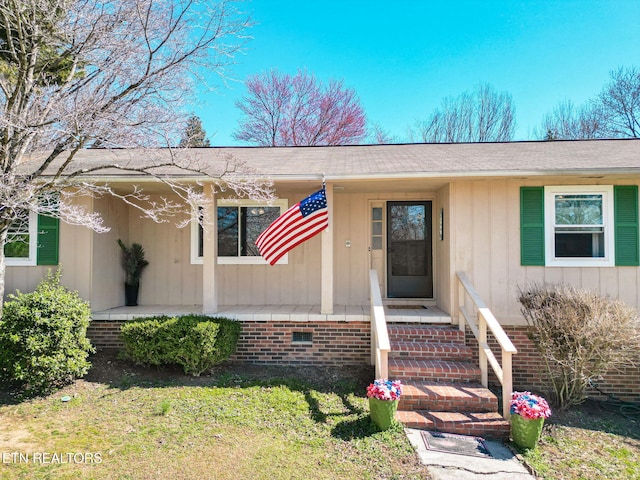 entrance to property featuring covered porch, crawl space, board and batten siding, and a lawn